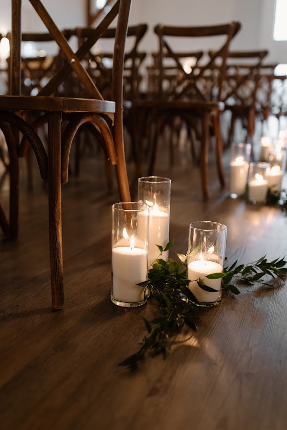 Hurricane candles and greenery lining the aisle for wedding ceremony