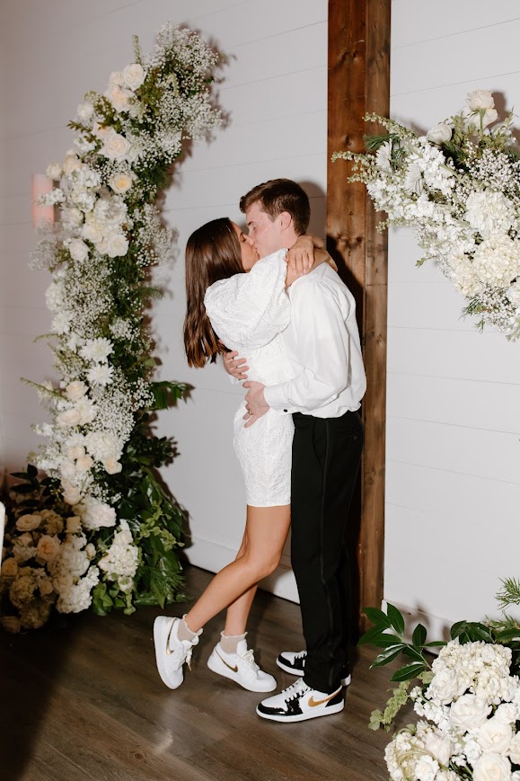 Kansas City wedding florist - Bride & Groom kissing in front of white wedding floral arch