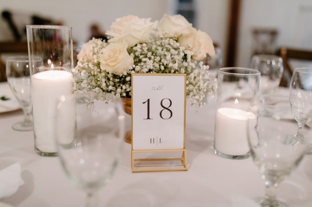 KBaby's breath and white roses centerpiece with candles and table number at wedding reception